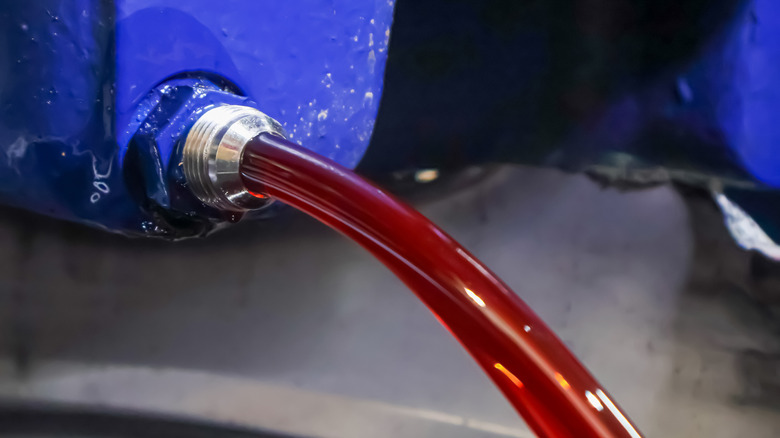A close-up view of a steady stream of red transmission fluid or hydraulic