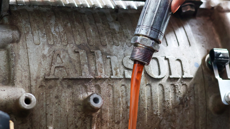 A mechanic is pouring bright red transmission fluid into a metallic engine