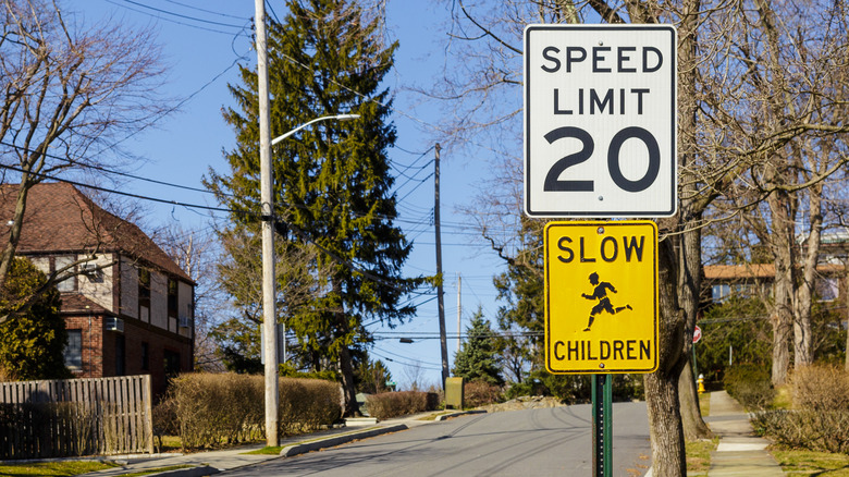 Yellow slow children at play sign below white speed limit sign on suburban street