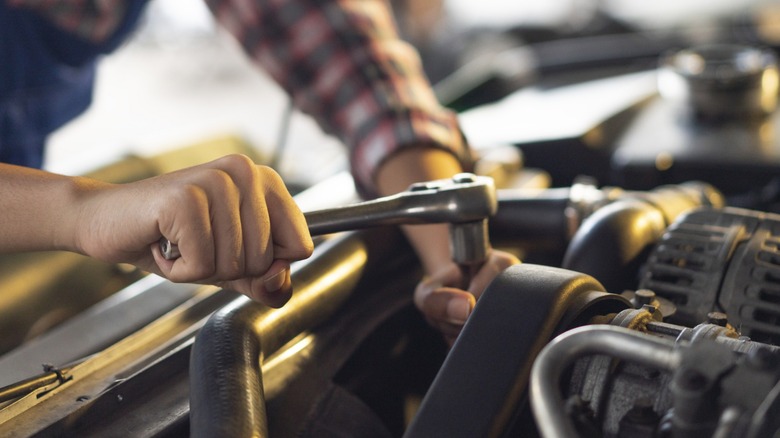 a person using a ratchet on a car's engine bay