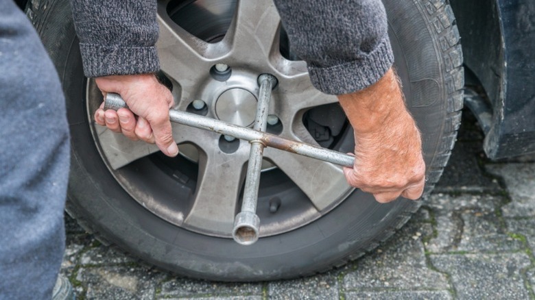 a person using a four-way socket wrench to remove wheel lug nuts