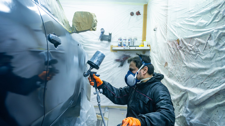 Man with a respirator on spraying paint onto a car