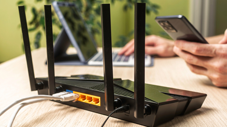 Close up router with two Ethernet cables attached, in the background a man works on a smartphone and a laptop