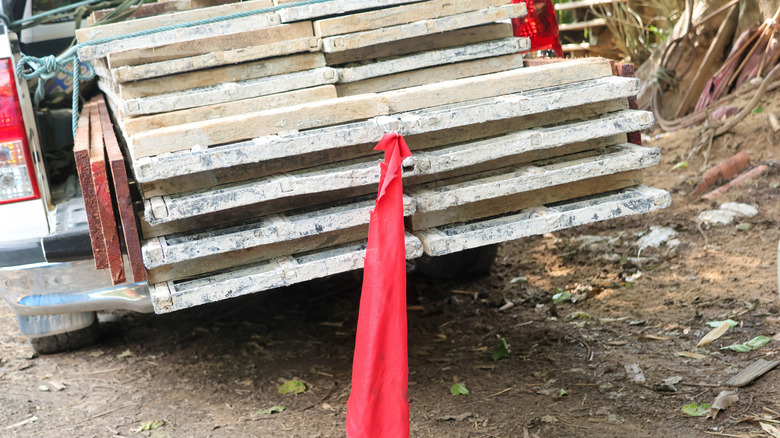 A pickup truck hauling planks with a red warning flag on the back.
