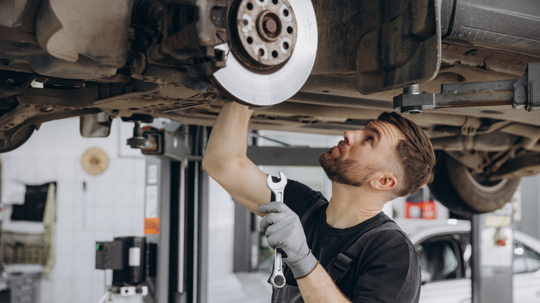 Male mechanic in uniform and gloves standing under a car