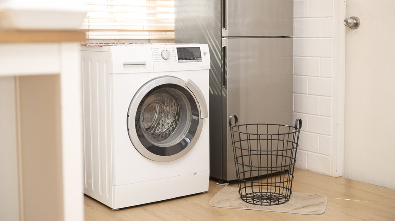 Washing machine installed against wall, refrigerator and laundry basket next to it