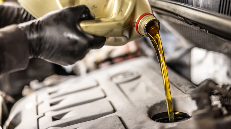Person with rubber gloves pouring motor oil into an engine