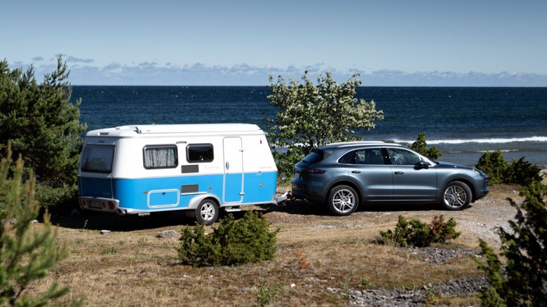 Wide angle shot of a 2019 Porsche Cayenne towing a camper van across a dirt trail.