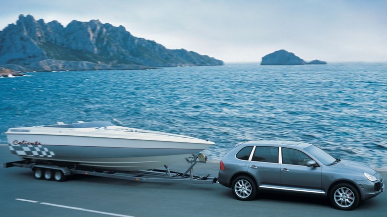 Side shot of a first-gen Porsche Cayenne towing a boat around a lake.