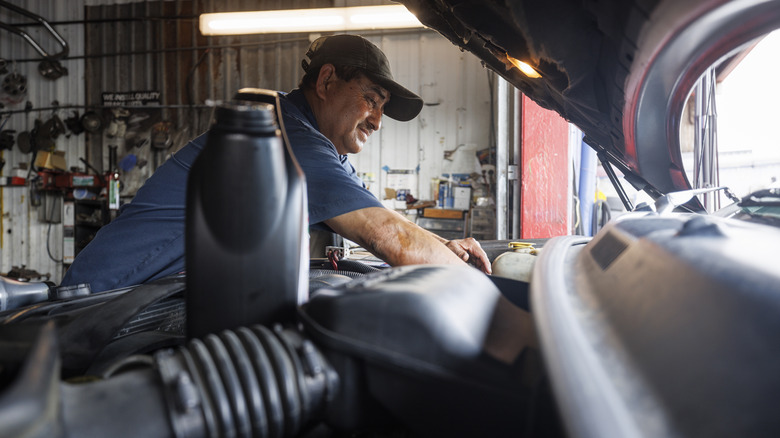 A mechanic leaning in a car's hood over the engine bay.
