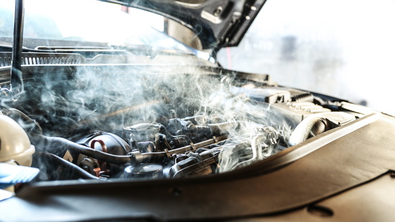 An overheating car engine smoking from the engine bay with its hood open.