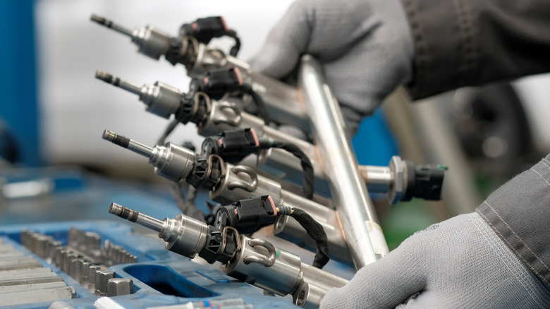 Gloved hands holding a fuel injection rail for a modern engine