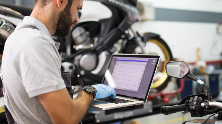 A mechanic diagnosing a motorcycle on a laptop