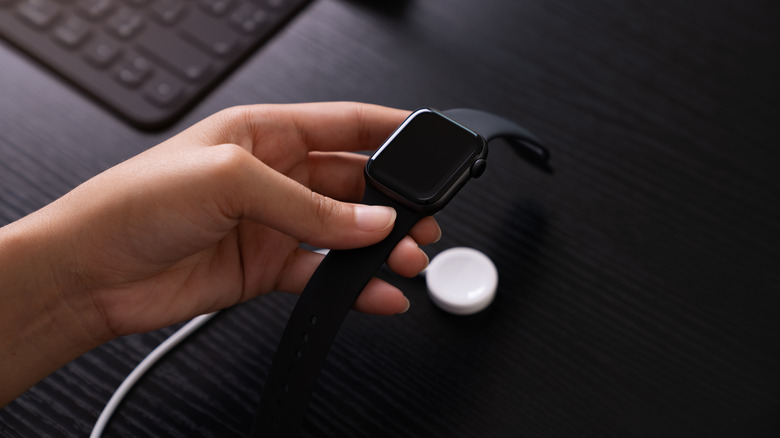 A person holding Apple Watch next to its charger
