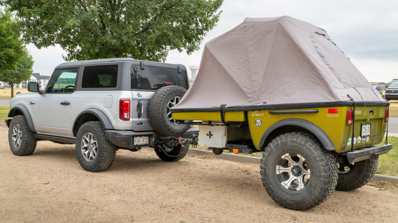A parked Ford Bronco with a trailer attached off-road.
