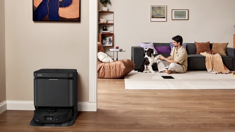 Eureka J15 Max Ultra and base station in a living room where a man plays with a pet dog