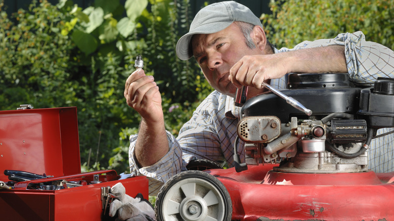 Close-up of man holding a spark plug with his lawn mower