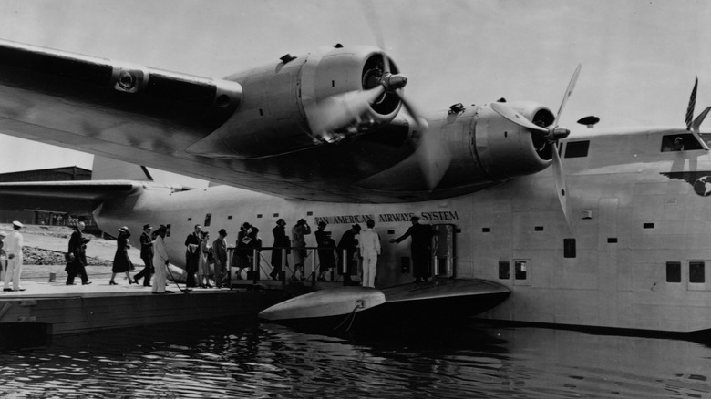 Passengers boarding Boeing 314 Clipper while it sits at a seaplane port
