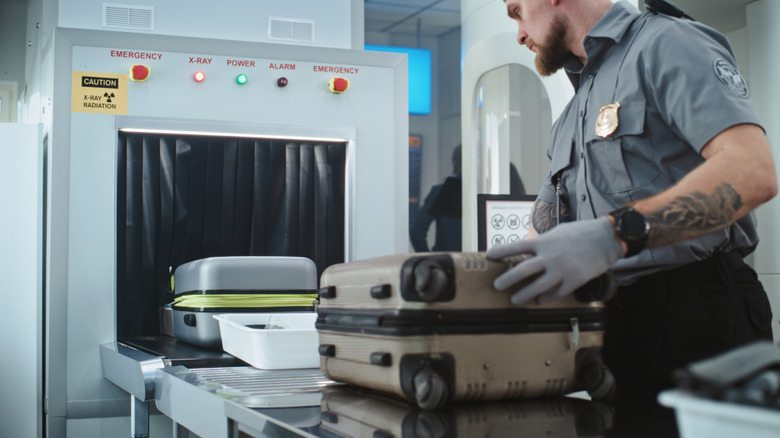 TSA employee prepares bags for x-ray machine.