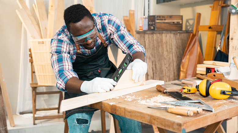A man with protective gear measuring some wood in a woodworking shop