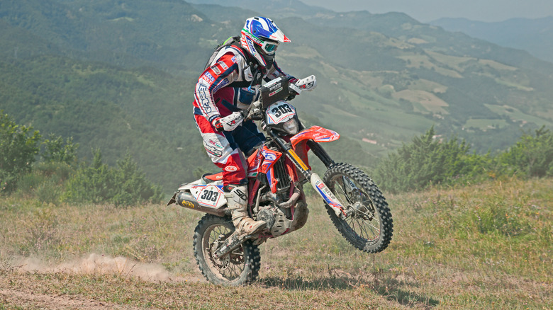 Man riding a Beta dirt bike off-road on a grassy trail.