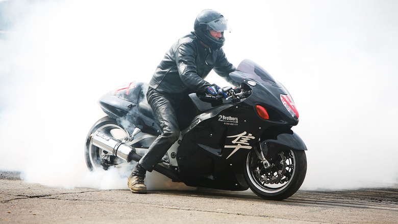 A rider doing a burnout on a modified black Suzuki Hayabusa