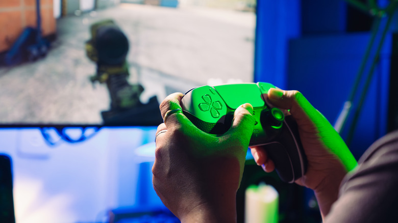 Hands holding a PS5 controller and playing FPS game
