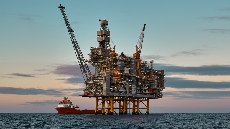 an offshore oil rig in the middle of the sea, with a supply vessel next to it