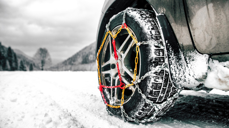 A close-up of a front left tire of a vehicle with tire chains.