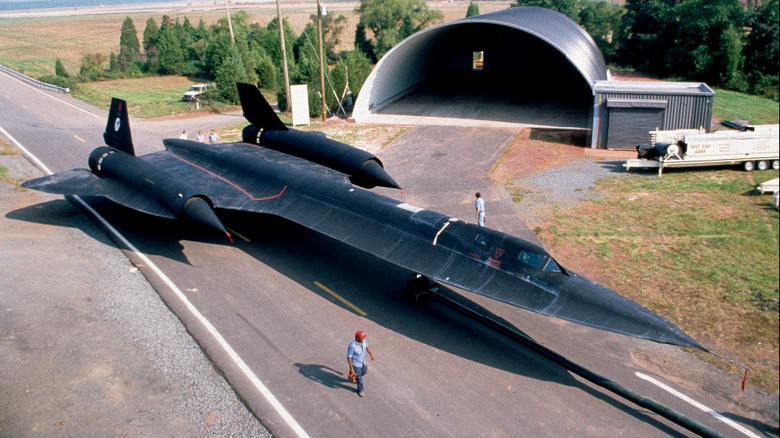 Ariel three-quarter view of SR-71 Blackbird supersonic plane next to a hangar.