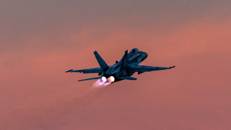 A F/A-18 is silhouetted against an orange sky as it takes flight