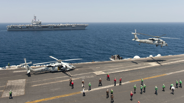 Aircraft and personnel on an aircraft carrier, with another carrier in the background.