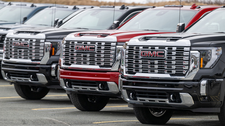Three brand new GMC vehicles parked in a row outside a dealer lot, two black, one red.