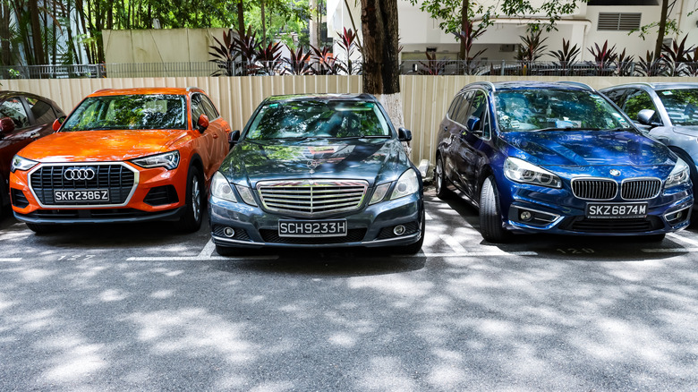 An orange Audi, black Mercedes, and Blue BMW parked at the side of street, in that order.