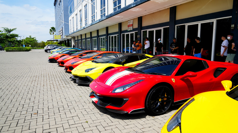 Several brightly-colored Lamborghinis in a row parked in front of a building, with a Ferrari in the foreground.