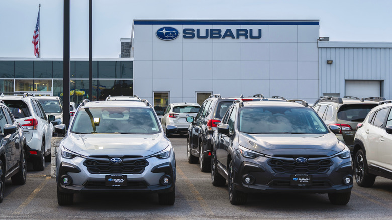 A white Subaru dealership building on a cloudy day with new Subaru cars in the foreground.