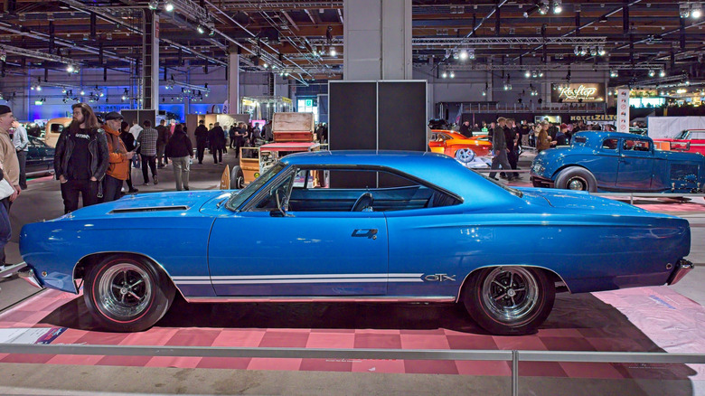 Side view of blue Plymouth GTX parked at indoor car show.