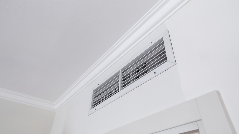 An AC vent shown near the ceiling of a white room