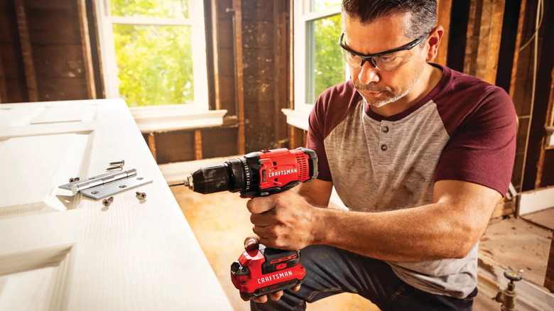 man using Craftsman cordless half-inch drill to put hinges on a door