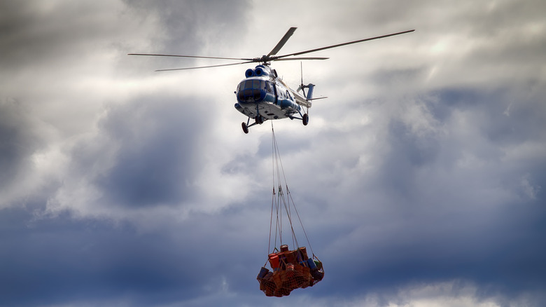A helicopter hauling several barrels within a cargo net