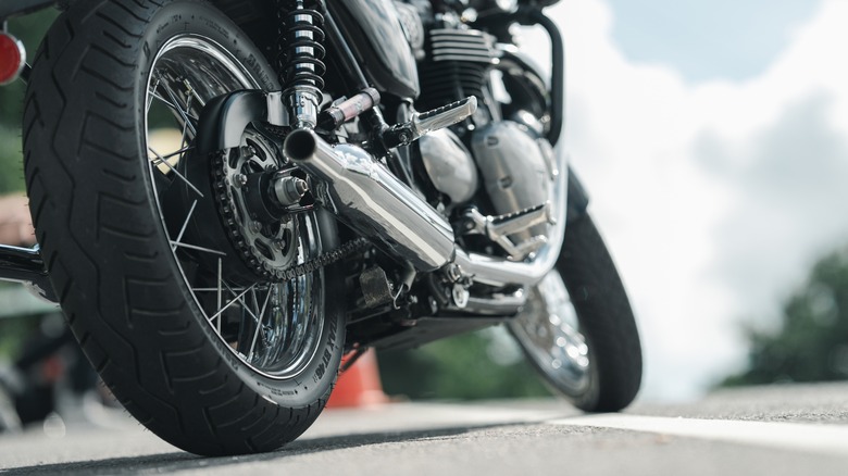 Dramatic, low angle shot of a parked motorcycle with focus on rear tyre and muffler, with road markings.