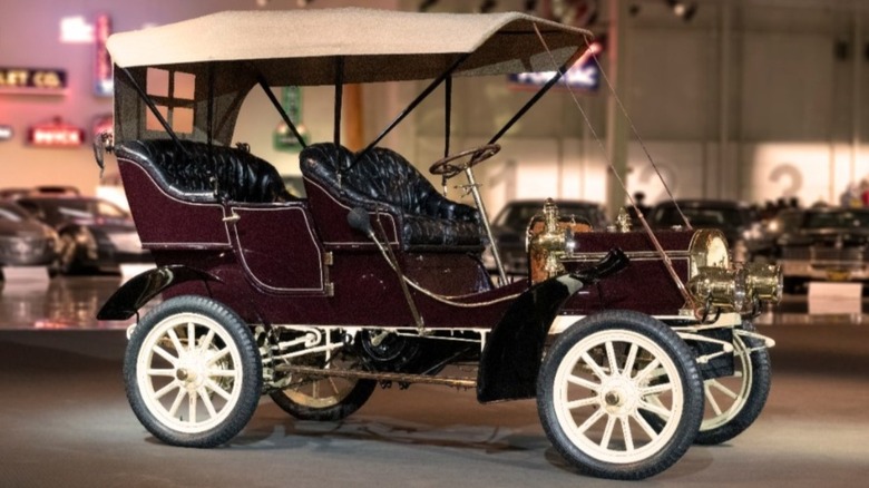A 1905 Buick Model C parked indoors with other cars in the background.
