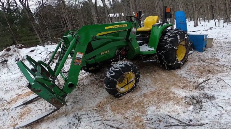 A John Deere 3038E tractor in snowy woodlands.