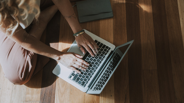 Woman using a MacBook laptop while sitting on the ground