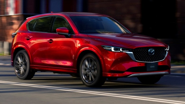 2025 Mazda CX-5 driving down city street with buildings in the background