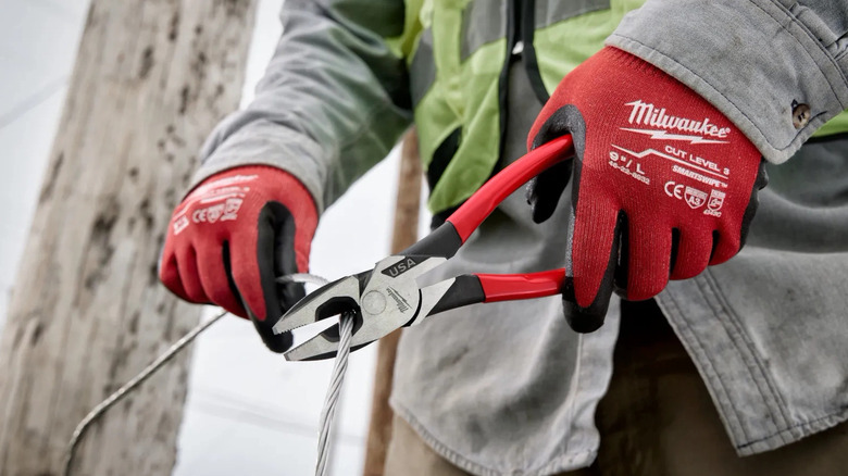 Person with red Milwaukee gloves using pliers on wire