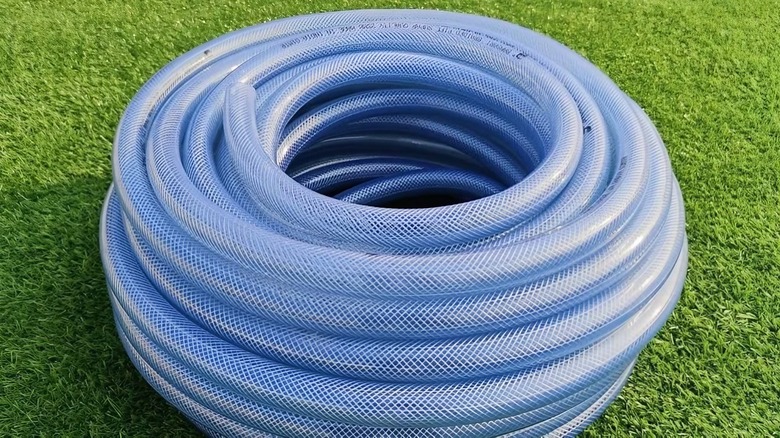 A Sylix High Pressure Braided Clear Flexible PVC hose, coiled up on a grass lawn