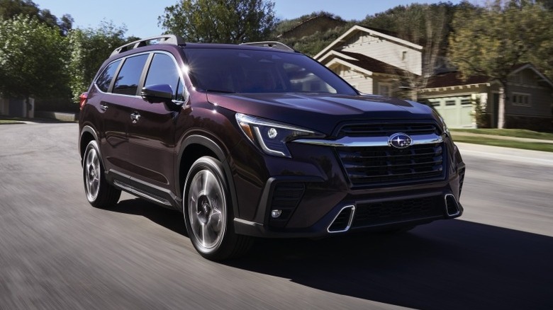 Subaru Ascent driving down a road with trees and buildings in the background