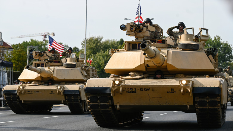 A pair of M1A1 Abrams tanks with the American flag driving on road