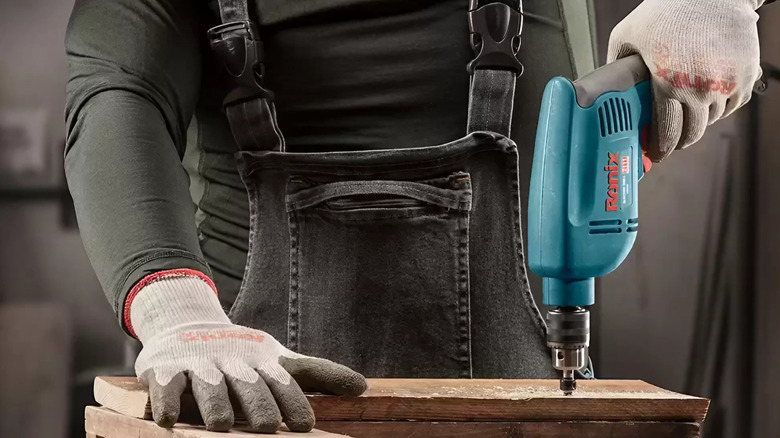man operates an electric drill on wood
